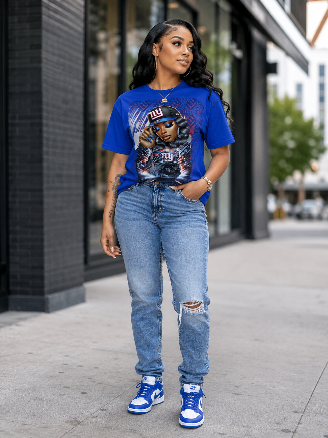 Woman wearing a blue graphic t-shirt and jeans standing on a sidewalk.